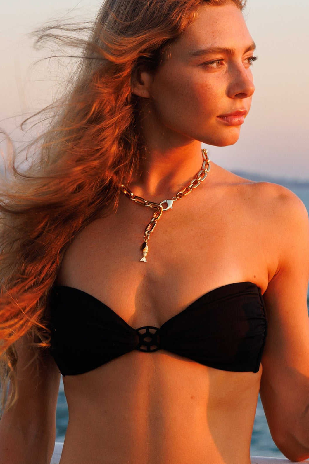 Woman in a black bikini holding a bottle by the sea at sunset